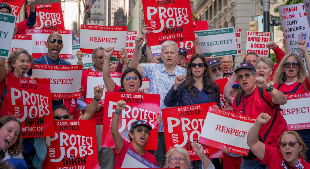 Large group of PSC members holding protest signs on Wall Street