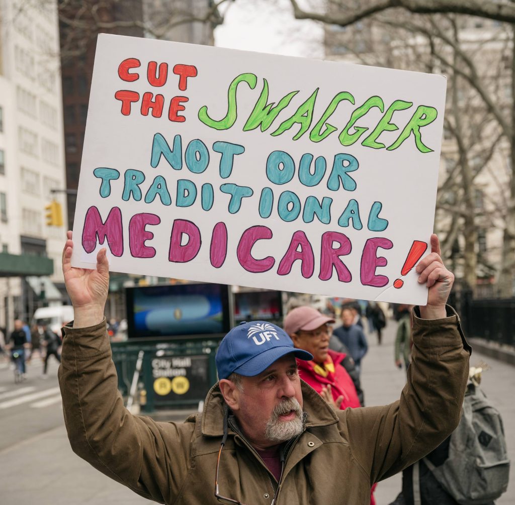 Man rallys with a sign: "Cut the swagger not our traditional medicare!"