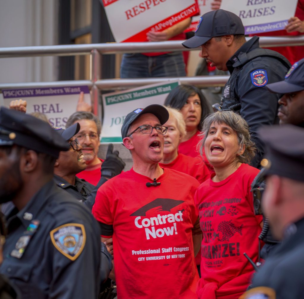 PSC President James Davis is arrested by NYPD officers while chanting and wearing a red "Contract Now!" t-shirt