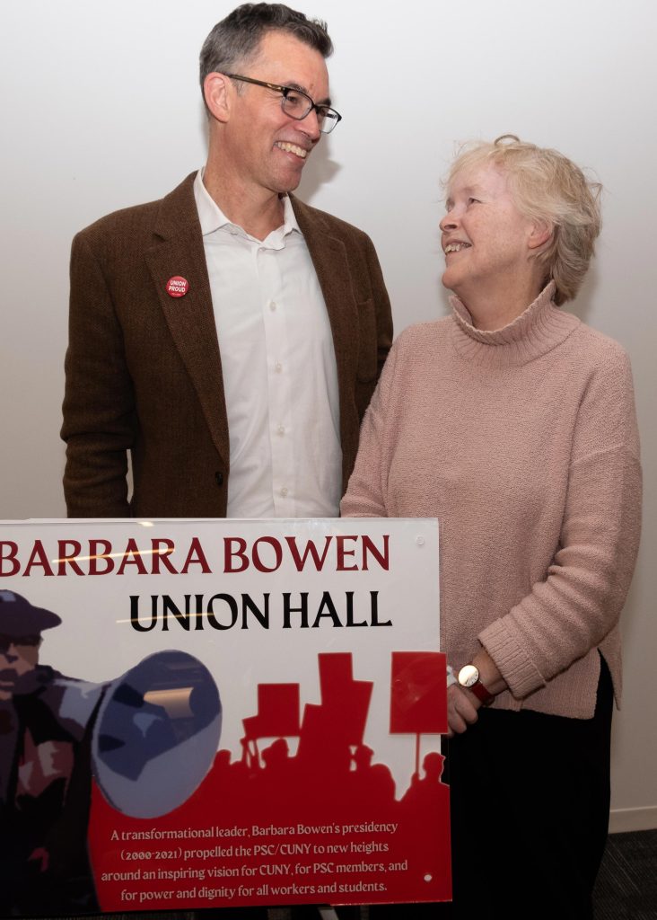 Two unionists smile near a plaque declaring "Barbara Bowen Union Hall"